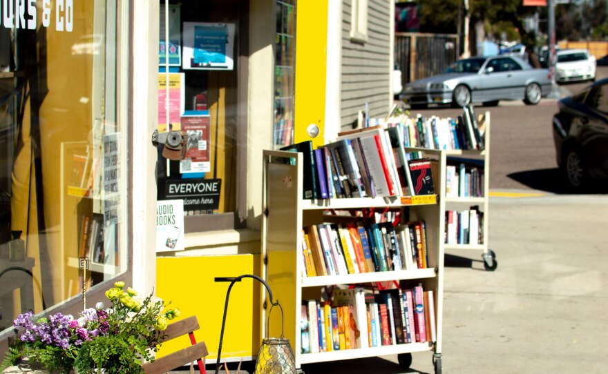 Libélula Books pictured from the sidewalk, with a yellow door and two carts of books outside.