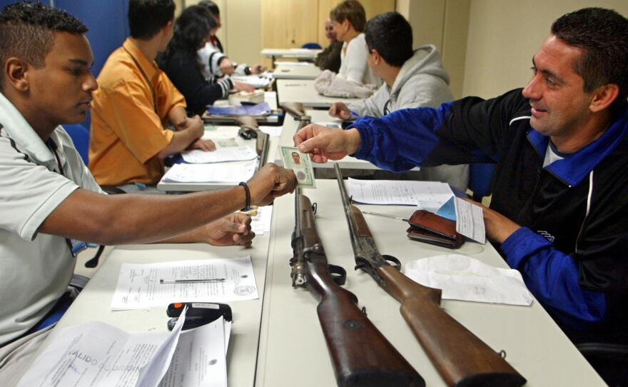 A Brazilian citizen shows his identification card to a Federal Police agent (left) as he trades in two collection rifles as part of a national firearm buyback program, in São Paulo, Brazil, July 23, 2004.