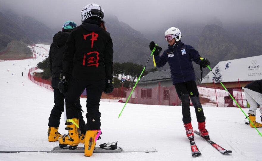 A skier gestures to others, one wearing a suit with the characters reading "China", on the slope of the Vanke Shijinglong Ski Resort in Yanqing on the outskirts of Beijing, China, Thursday, Dec. 23, 2021.
