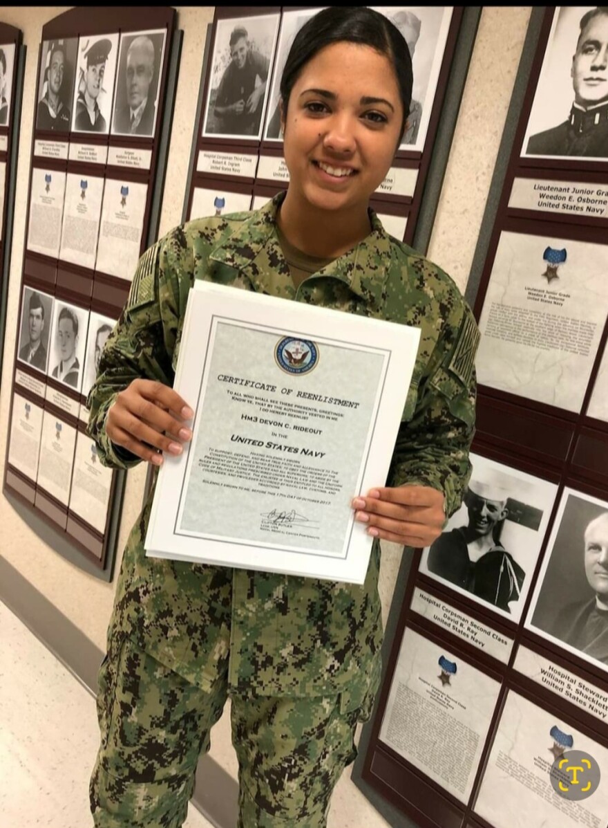Petty Officer 3rd Class Devon Rideout stands in a hallway in her green camouflage uniform holding her certificate of reenlistment in an undated photo.