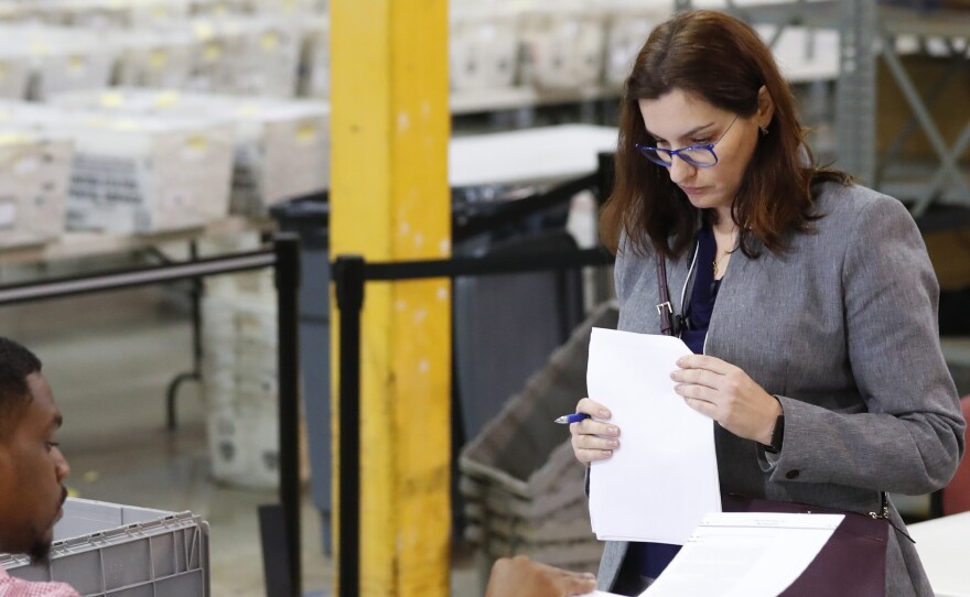 A Republican party observer, right, watches as an employee at the Palm Beach County Supervisor Of Elections office goes through a stack of damaged ballots, Thursday, Nov. 15, 2018, in West Palm Beach, Fla.