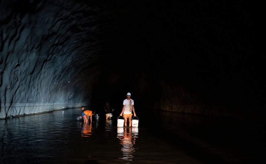 Residents of the El Cardon community, who do not receive drinking water at home, carry buckets and drums with water collected from a natural pond formed in a tunnel in Caracas, Venezuela.