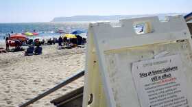 A sign in Coronado reminding residents the stay at home guidance is still in effect as people lounge on the beach on July 12, 2020.