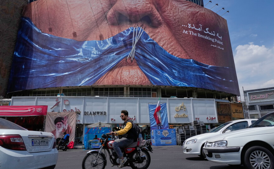 Vehicles drive past a billboard with an illustration showing the Strait of Hormuz and the sewn lips of President Trump in a square in downtown Tehran, Iran, May 2.