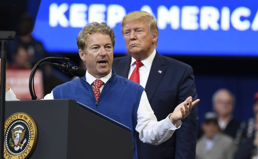 President Trump listens Monday as Sen. Rand Paul, R-Ky., speaks during a campaign rally in Lexington, Ky., in which Paul called on the media to release the name of the whistleblower.