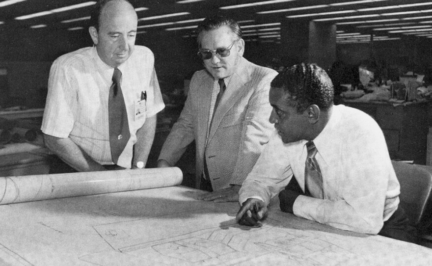 Chuck Lowry (left) reviews designs on a drafting board with Carlos Moore and Kel Shaw (right).