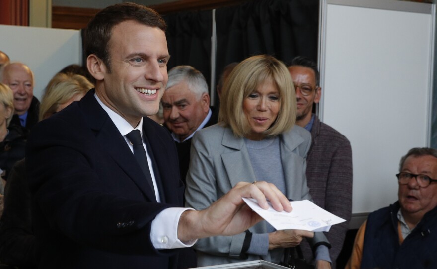 French presidential election candidate for the En Marche ! movement Emmanuel Macron (L) stands next to his wife, Brigitte Trogneux as he casts his ballot at a polling station in Le Touquet, northern France, on April 23, 2017, during the first round of the Presidential election.