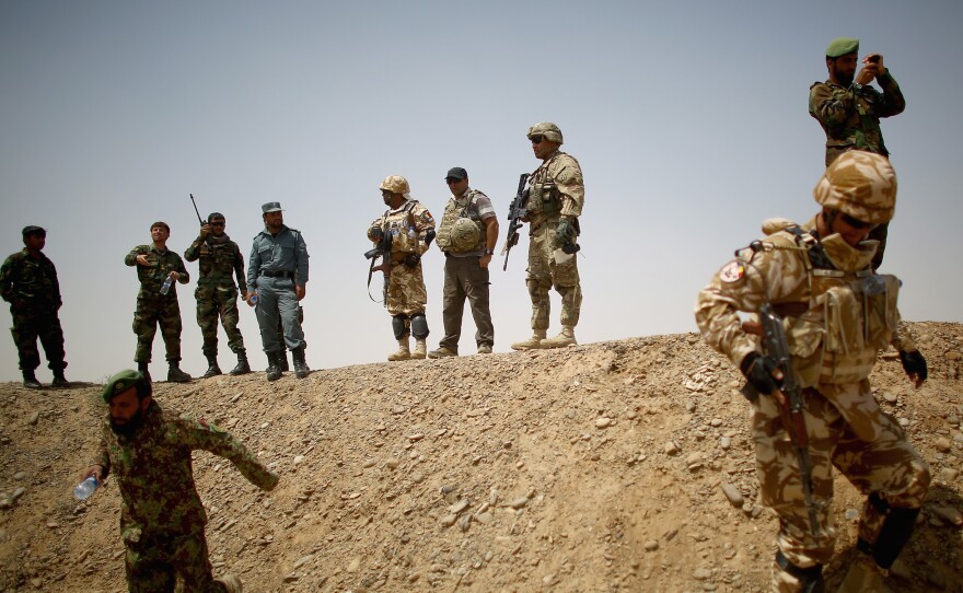(Top) Afghan, U.S. and Romanian soldiers on a berm at the Tarnak Training Range, where they are learning to use artillery. (Left) An Afghan soldier runs toward a mortar with a practice "round" — a water bottle. (Right) U.S. Army trainer Maj. Kevin McCormick talks with Afghan army 1st Lt. Hayatullah Froton during an artillery training exercise.
