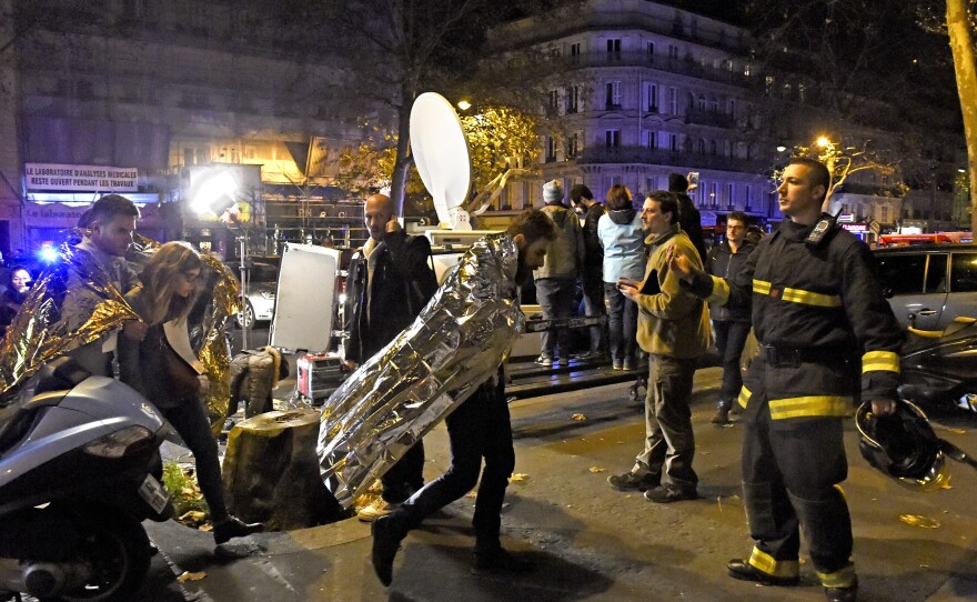 People wearing survival blankets walk by a rescuer near the Bataclan concert hall.