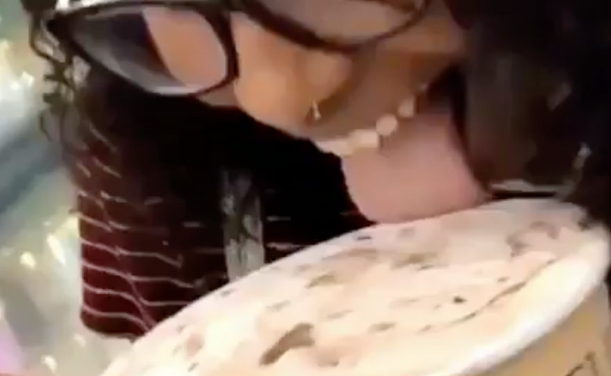 A screenshot of a video shows a young woman opening a carton of ice cream, licking it and putting it back in the grocery store case.