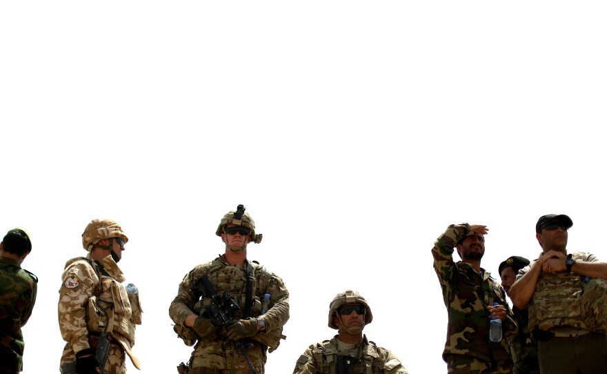 American, Afghan and Romanian soldiers watch as a mortar round flies through the air to its target.