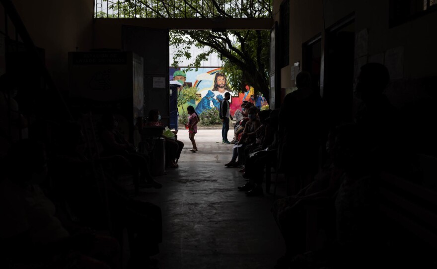 People wait outside the medical clinic of the priest and doctor, Raymond Portelli, located in the San Martin de Porres church in Iquitos, Peru. Portelli sees 30 patients a day and says he now rarely sees COVID cases.