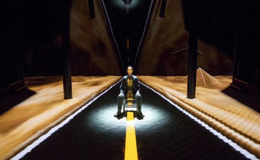 The set for <em>Grounded</em> consists of little more than a layer of sand, a metal chair and a background of black reflective glass.