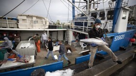 Fishing boat captain Nick Haworth, right, carries tuna to a dock for sale Friday, March 20, 2020, in San Diego. Haworth came home to California after weeks at sea to find a state all but shuttered due to coronavirus measures, and nowhere to sell their catch. A handful of tuna boats filled with tens of thousands of pounds of fish are now floating off San Diego's coast as they scramble to find customers. Haworth was selling on Friday to individuals for less than half what he would get from wholesalers. "This is a quarantine special," he joked. 