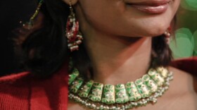Film still of woman wearing an emerald necklace. “Illusions In Stone” tells the global story of the emerald trade.