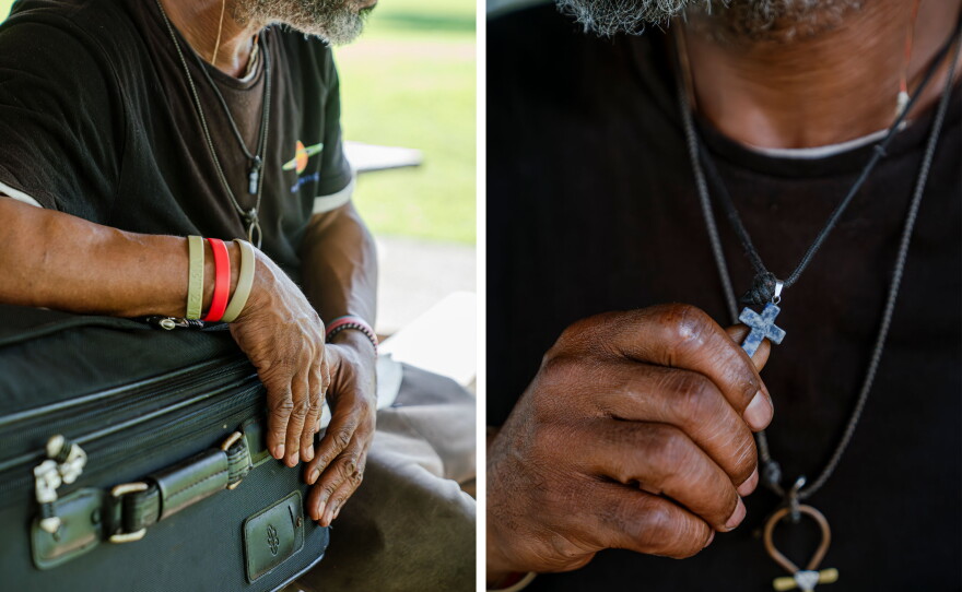 Joseph Williams holds a cross and rests his arm on top of his suitcase under the pavilion where he sleeps.