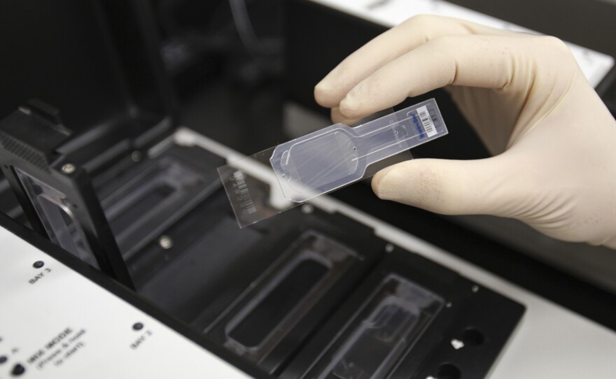 A biologist holds a slide prepared for testing in a micro array for biological hazards at the Lawrence Livermore National Laboratory in Livermore, Calif.