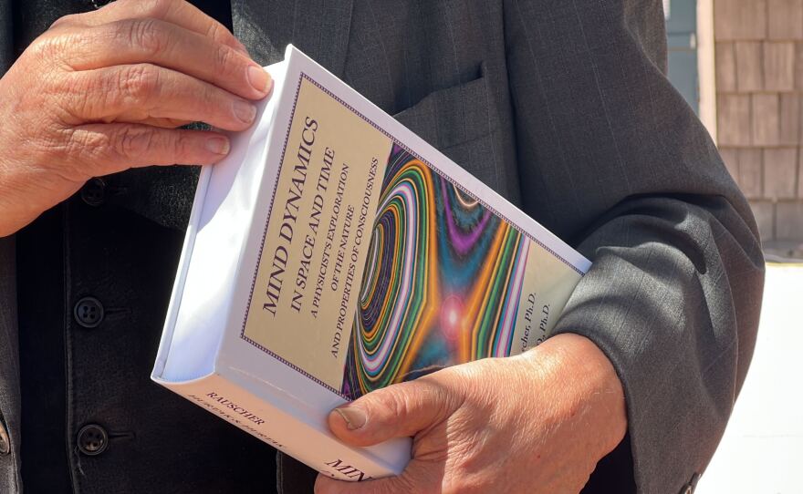 Conference speaker J.J. Hurtak, Ph.D. is shown holding his book "Mind Dynamics in Space and Time" at Marina Village in San Diego on April 21, 2023.
