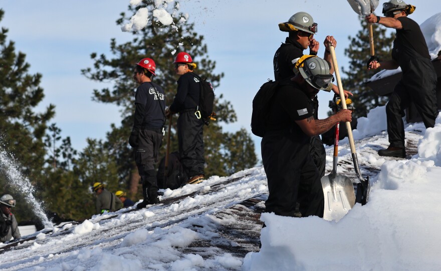 Members of the California Army National Guard Joint Task Force Rattlesnake shovel snow from a rooftop after a series of winter storms dropped more than 100 inches of snow in the San Bernardino Mountains in Southern California on March 8, 2023 in Crestline, California.