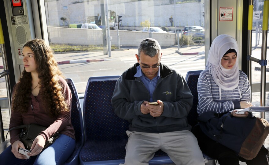 David Felber (center) rides the light rail, sitting between Israeli and Palestinian university students. He lives in East Jerusalem and opposed the rail's route through Palestinian neighborhoods, but is now a regular rider.