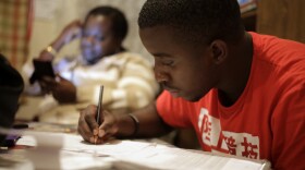 In this Wednesday, Nov. 15, 2017 photo, Amocachy Jeune, right, does homework as his mother Marianne Jeune, left, a Haitian immigrant staying in the U.S. through the Temporary Protected Status program, sits nearby at their Boston home.
