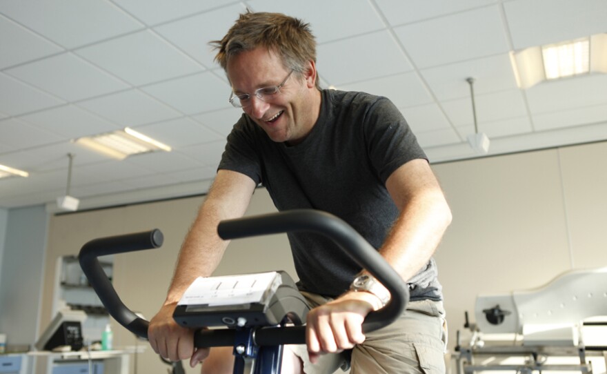 Dr. Michael Mosley on an exercise bike at University of Nottingham Medical School. He is performing his first ever session of High Intensity Training (HIT) on an exercise bike. Michael smiles as he is skeptical that cycling a total of three minutes a week can have just as many health benefits (if not more) than longer endurance training sessions.