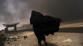 An Iraqi woman walks through a plume of smoke rising from a massive fire at a liquid gas factory as she searches for her husband in the vicinity in Basra, Iraq, May 2, 2003.