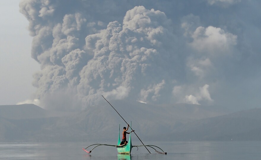 A boy who lives at the foot of Taal paddles an outrigger canoe while the volcano spews ash Monday.