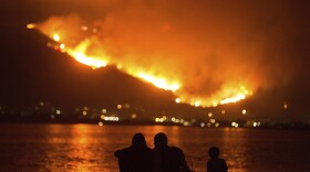 A family sits along the shore of Lake Elsinore as they watch the Holy Fire burn in the distance on Thursday night, Aug. 9, 2018. 