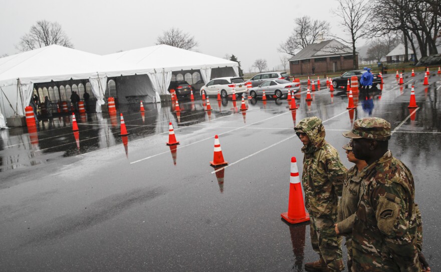 National Guard personnel stand beside a line of motorists waiting for coronavirus testing in New Rochelle, N.Y., on Friday. Major retailers such as CVS, Target and Walmart are pledging to set up drive- through test sites in some of their parking lots.