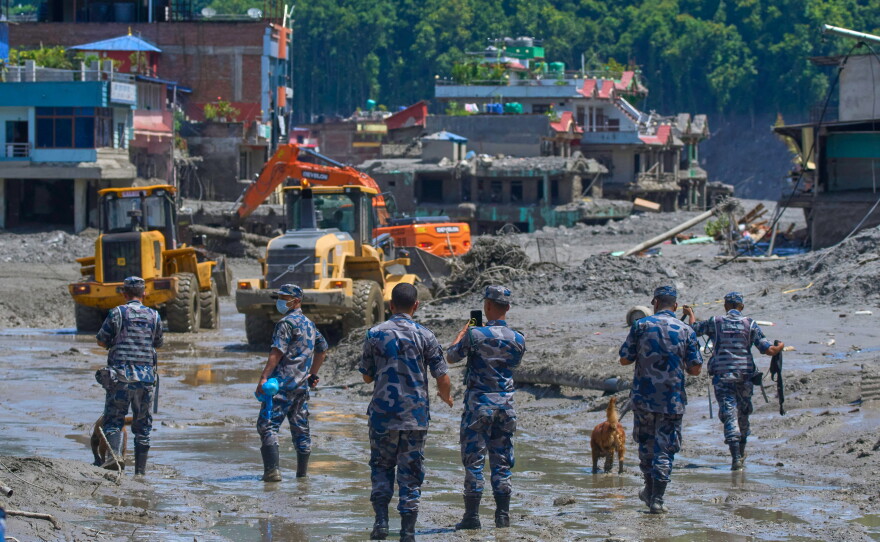 Nepalese policemen watch as earthmovers clear the debris of flash flooding in Nepal's Nuwakot district, Thursday, Aug. 27, 2026. (AP Photo/Niranjan Shrestha)