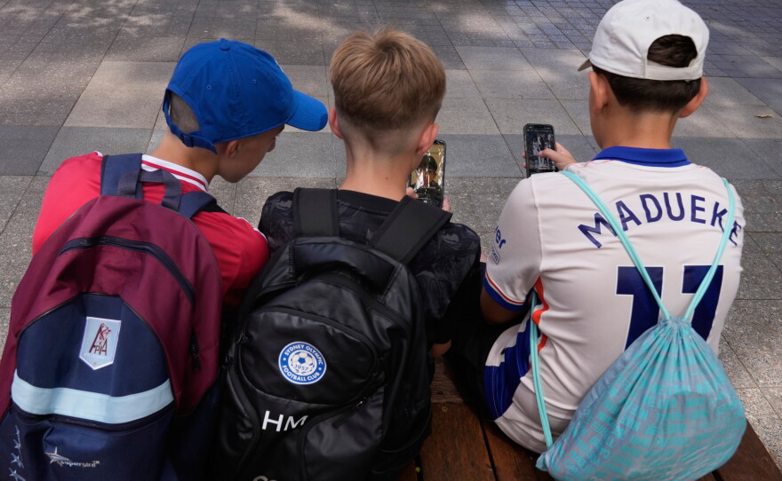 FILE - Three boys use their phones while sitting outside a school in Sydney, Monday, Dec. 8, 2025.