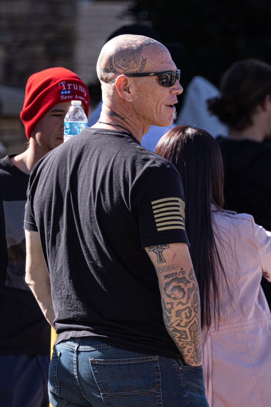 An anti-trans demonstrator who appears in several pictures with Navy SEAL Bryce Henson is shown here from the back where several Nazi symbols, including a swastika, are visible tattooed on his body.