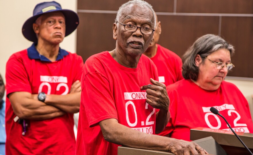 Robert Taylor, center, speaks at a St. John the Baptist Parish council meeting in 2017. He and the other members of the citizens' group around him wear T-shirts that reference the safety limit for the chemical chloroprene.