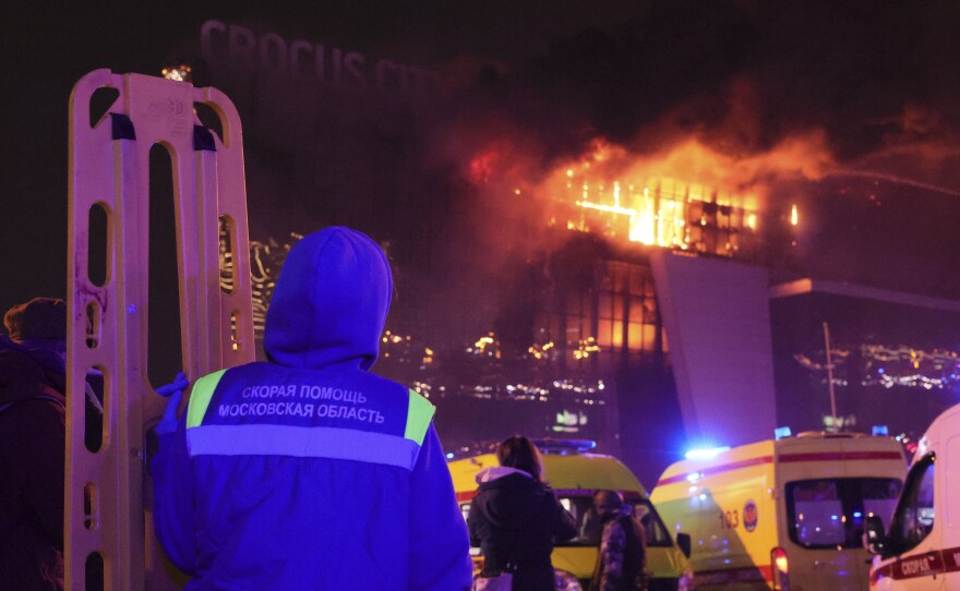 A medic stands near ambulances parked outside the burning building of the Crocus City Hall on the western edge of Moscow, Russia, Friday, March 22, 2024. Several gunmen have burst into a big concert hall in Moscow and fired automatic weapons at the crowd