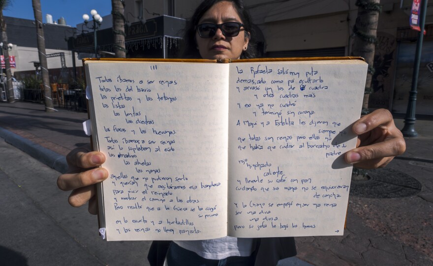 While standing on Tijuana's Avenida Revolución, poet Sofía Favela Magro holds her notebook up with a handwritten untitled poem, Dec. 6, 2024. The poem starts: Todas íbamos a ser reinas. Todas las del barrio. Las prietas y las tetonas. Las listas. Las lentas. Las diestras."