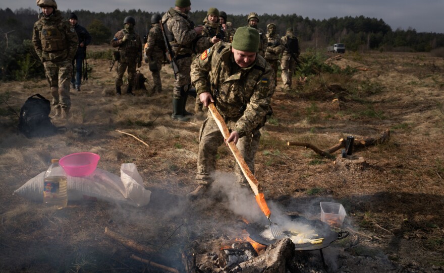 A soldier fries potatoes over a fire.