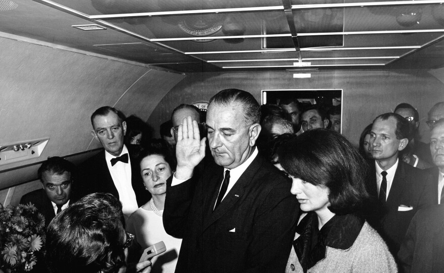 President Lyndon B. Johnson takes the oath of office on Air Force One at Love Field in Dallas, Texas, following the assassination of President John F. Kennedy' 1963. Left to right: Assistant Press Secretary, Malcolm Kilduff (holding dictating machine, partially out of frame); Judge Sarah T. Hughes (administering oath); Jack Valenti; Congressman Albert Thomas of Texas; Secretary to President Johnson, Marie Fehmer (partially hidden behind Thomas); First Lady Lady Bird Johnson; Dallas Police Chief, Jesse Curry (face hidden by Vice President’s raised hand); President Johnson; Secretary to President Kennedy, Evelyn Lincoln (mostly hidden behind Mrs. Kennedy); Congressman Homer Thornberry of Texas (mostly hidden behind Lincoln); Secret Service agents Roy Kellerman (partially hidden behind Thornberry) and Thomas “Lem” Johns (partially hidden behind Mrs. Kennedy); former First Lady Jacqueline Kennedy; Mrs. Kennedy’s Press Secretary, Pamela Turnure (partially hidden behind Brooks); Congressman Jack Brooks of Texas; deputy director of public affairs for the Peace Corps, Bill Moyers (mostly obscured by Brooks); President Kennedy’s physician, Admiral Dr. George G. Burkley (on edge of frame); others in background.