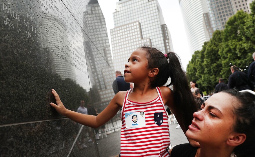 Bernadette Ortiz holds her daughter, Adriana, last year as she looks for the name of her grandfather, New York City Police Officer Edwin Ortiz, at a wall commemorating fallen officers in New York City. Families gathered at the wall following a procession in Lower Manhattan to mark the anniversary of the Sept. 11 attacks and honor officers who were killed.