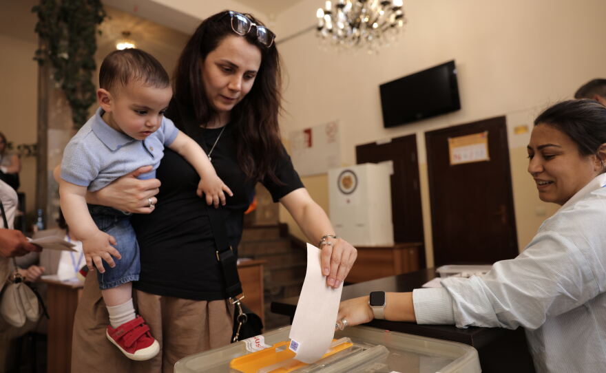 A woman holding a child casts her ballot at a polling station during a parliamentary election in Yerevan, Armenia, Sunday, June 7, 2026.