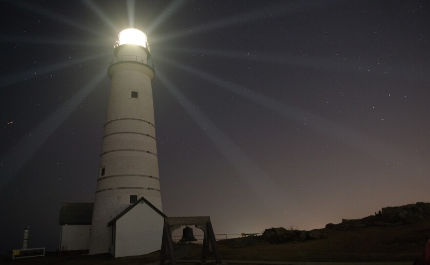 Boston Light, America's first lighthouse, beams light across the night sky.