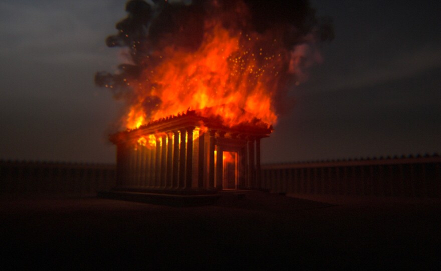 Computer-generated imagery of the Temple of Eleusis, a pilgrimage site in ancient Rome, engulfed in flames.