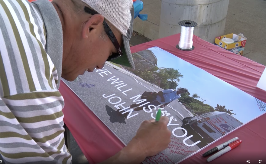 A well-wisher signs a photo poster of retired mail carrier John Piontek in his uniform. Photo taken June 30, 2021.