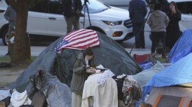 In this March 24, 2021, file photo a woman eats at her tent at the Echo Park homeless encampment at Echo Park Lake in Los Angeles.