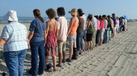 Following an interfaith service in Grand Isle, La., people gather at a berm overlooking the ocean and hold hands.