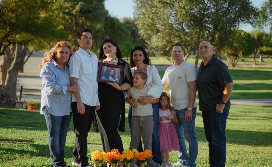 From left, Julie Estrada, Matthew Estrada, Cheyenne Estrada, Brandie Curtis, Cash Curtis, Illiana Curtis, Jeff Curtis and Larry Estrada stand for a portrait behind Ciara Estrada's grave at the Murrieta Valley Cemetery District in Murrieta, California on Oct. 4, 2025. (Kori Suzuki / KPBS)