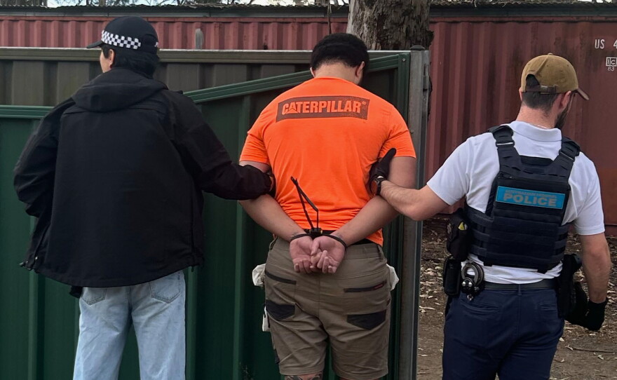 In this photo provided by the Australian Federal Police, a man, center, is arrested by police in Londonderry in western Sydney, Friday, June 19, 2026.