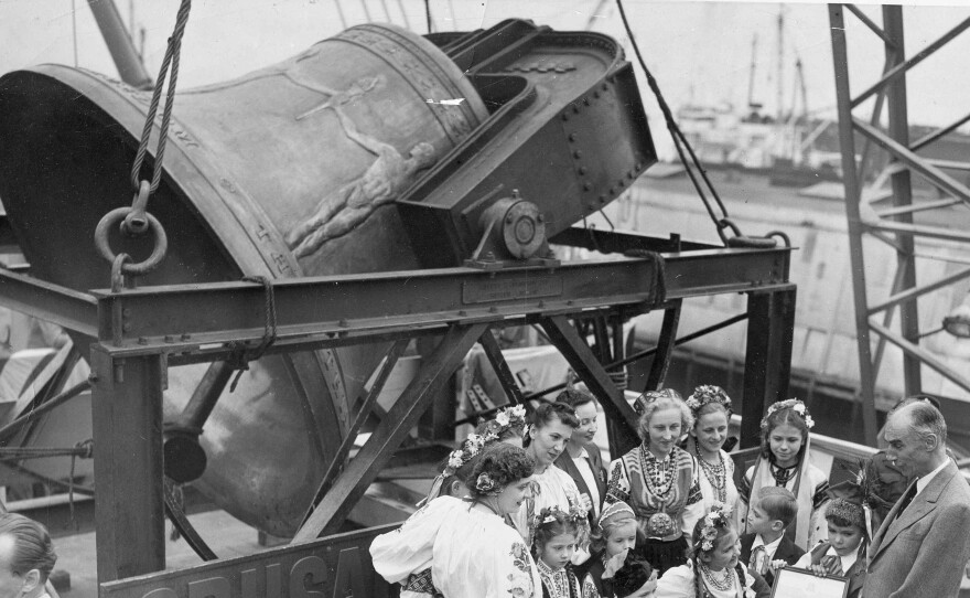 A group of former displaced persons helps to load the Freedom Bell aboard a Navy transport vessel in Brooklyn, New York, Oct. 9, 1950. One of the children, Eva Zandler, 8, originally from Poland, presents a scroll to be enshrined in the Freedom Bell Tower in Berlin, to Frederick Osborn, New York City chairman for the Crusade for Freedom.
