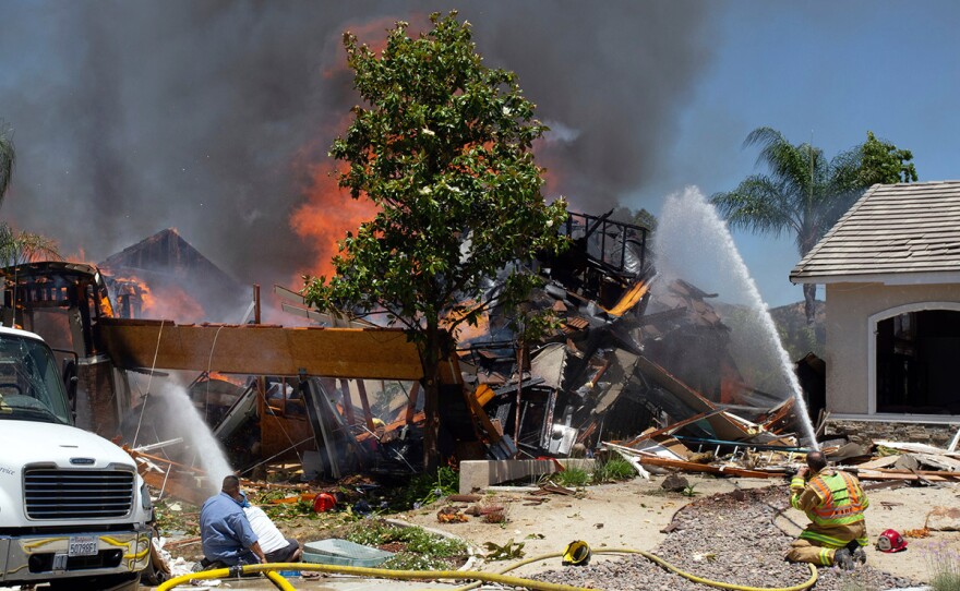 A firefighter and civilians train fire hoses on a burning home after an explosion and fire destroyed the home in Murrieta, Calif., sending up thick flames and closing several streets. One Southern California Gas Company employee was killed. 