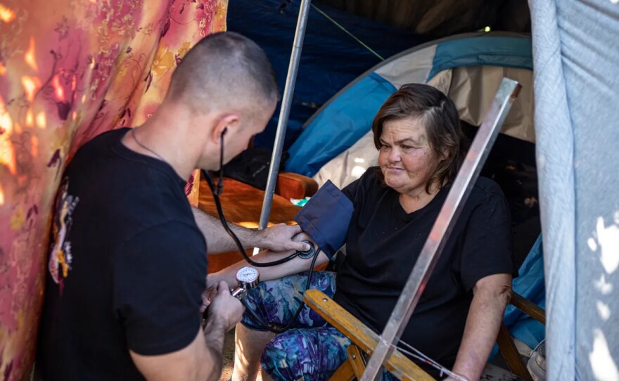 Physician assistant Brett Feldman checks Carla Bolen’s blood pressure at her encampment on the Figueroa Street Viaduct above Highway 110 in Elysian Valley Park in Los Angeles on Nov. 18, 2022.
